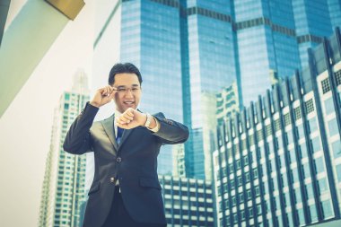 Yakışıklı bir işadamı kol saati zaman kontrol etmek için arıyor. Zamanında buluşma noktası için geldiği zaman sevimli yakışıklı adam mutlu hissediyor. Onun gülümseme olacak. Cityscape arka plan ile tam takım elbise giyiyor