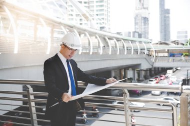 İcra veya mühendis adam blueprint arıyor. Yakışıklı erkek takım elbise, kravat ve baret giy. O uzman veya profesyonel yapı yüksek bina. O memnun proje veya işine bak. kopya alanı