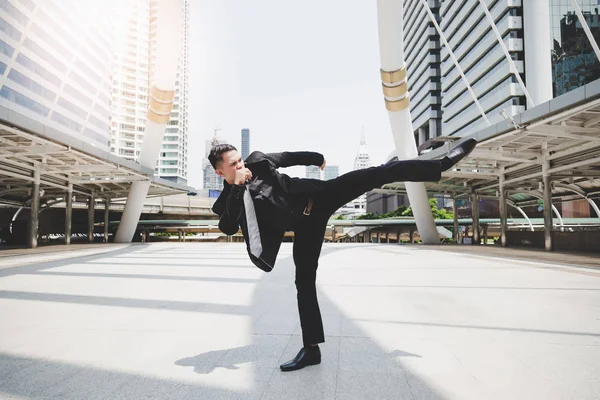Handsome businessman get angry his boss and wants to relieve stress and furious. Cool guy is exercising by kicking on the air. Attractive man wears suit, necktie, long trousers. cityscape background
