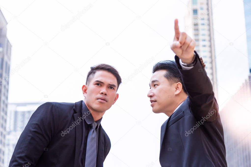 The guy is telling the way to handsome young businessman and pointing finger to the destination. Young guy is looking for new office. It is the first time he comes to the city and gets confused the way