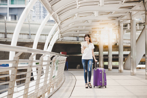 Обаятельная красивая женщина смотрит на карту, чтобы найти пункт назначения. Привлекательная девушка путается в большом городе. Красивая девушка ходит по улице и таскает чемодан. У неё длинные выходные.
