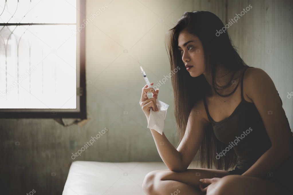 Drug addict woman look at hypodermic syring, contain heroin, cocaine and preparing inject drug into arm veins. She is a drug dealer also. Narcotic is unhealthy for body, ruin her life. room background