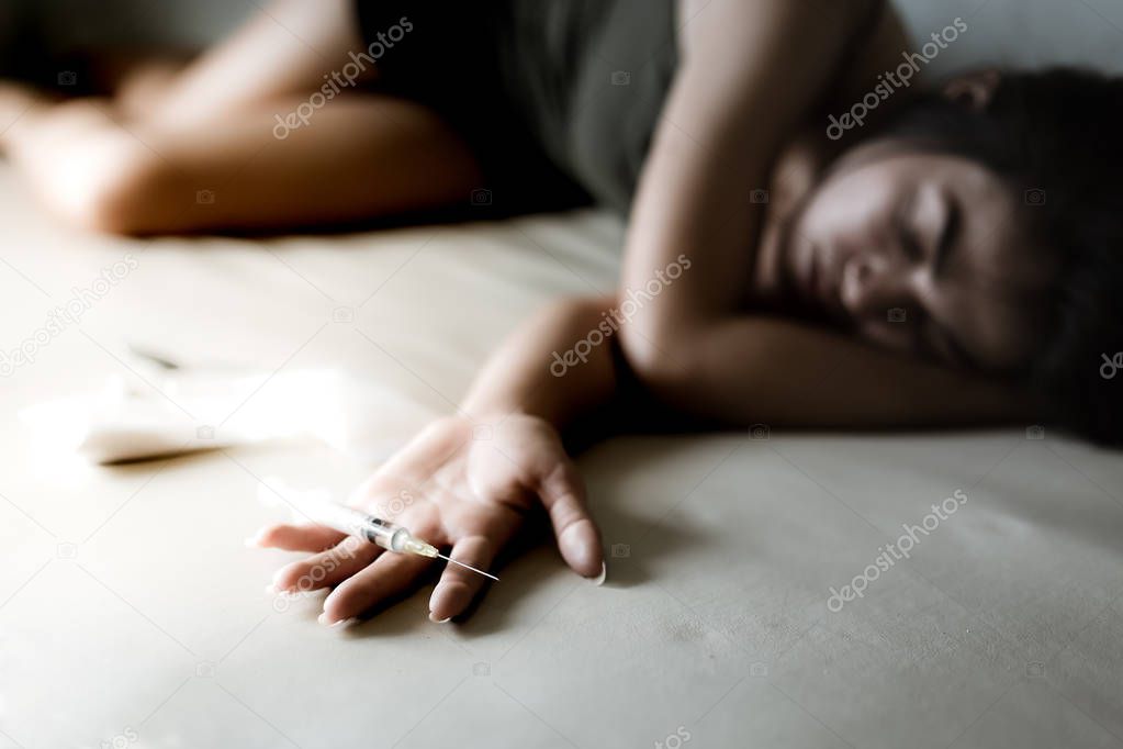 The junkie woman or drug addict girl is putting hand on bed and puts injection needle contain heroin or narcotic on her hand. Poor girl lay down on bed and get drunk or unconscious at dark room.