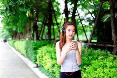 Güzel genç kadın çekici güzel Asya kadın sabah egzersiz için koşu yaparken bir parkta güzel müzik arama için smartphone bakıyor. Mükemmel vücut çekici güzel kız var