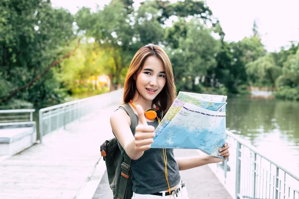 Portrait beautiful asian traveler woman. Asian young girl gives thumb up to someone. Pretty girl holds a map for finding tourism location. Attractive woman gets happy and satisfied of her tourism.