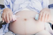 Atraktivní krásná těhotná žena drží lahve od mléka a působí jako krmení dítěte nebo plod v břiše v nemocničním pokoji. Krásná matka má dvojče miminka. Má pocit štěstí a radosti ze života