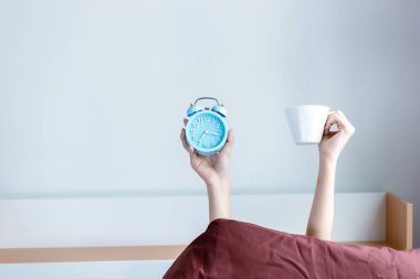 Çekici güzel kadın çalar saat ve bir fincan kahve holding ve sabah kahve zamanında olduğunu gösteren için havaya kaldırın. Güzel kız sabah kahve içmeyi seviyorum. kopya alanı