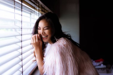 Portre sevimli güzel neşeli kadın. Çekici güzel kız bir şaka hikaye gülüyor. Muhteşem bir kadın kış sezonunda oturma odası pencereye yakın dur. Seksi Asyalı kadın komik kızdır