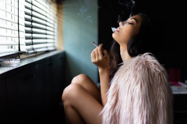 Güzel seksi kadın büyüleyici esrar veya sigara sigara içiyor. Çekici güzel kız hissediyorum rahatlatıcı ve mutluluk. O fikirli yok ya da rüya gibi bir durumda hissediyorum. Güzel Asyalı kadın giyim kürk manto