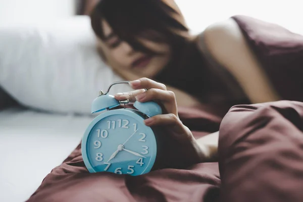 Alarm clock is alarming in morning for waking up beautiful woman that it is disturbing attractive beautiful girl. Charming beautiful woman does not want to get up, she feel tired. She try stopping clock