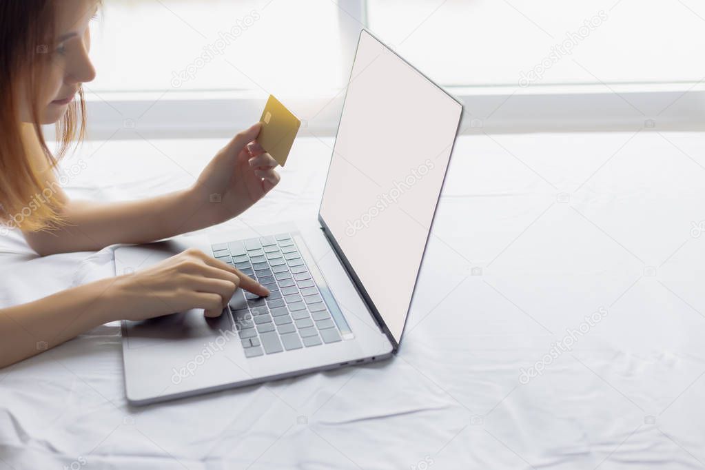 Attractive beautiful shopping woman is typing some information of her credit card on laptop keyboard. Gorgeous asian woman is doing financial on internet banking at bedroom. isolated or white screen