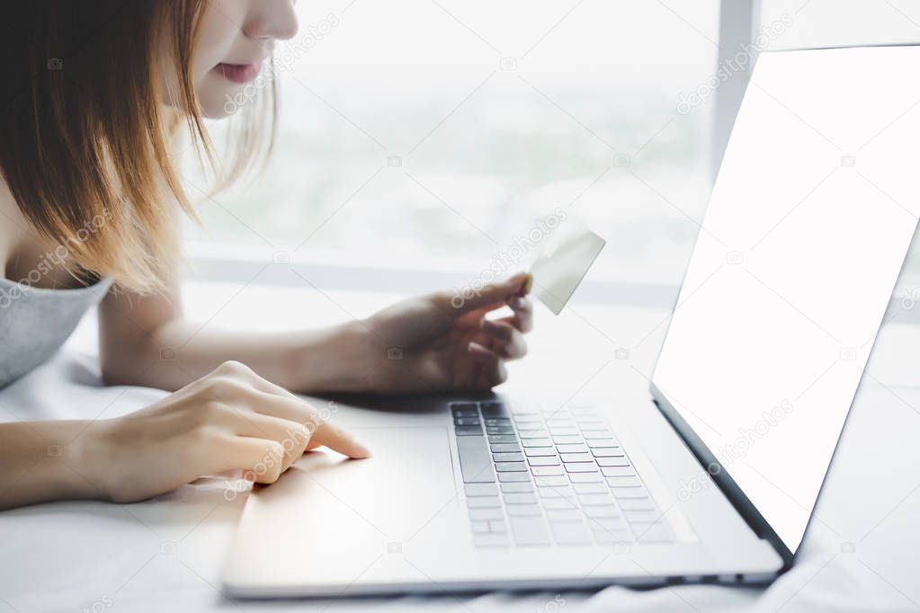 Attractive beautiful customer woman is searching and finding some financial banking for putting security code of credit card by using laptop, internet on her bed at home. white screen on laptop screen