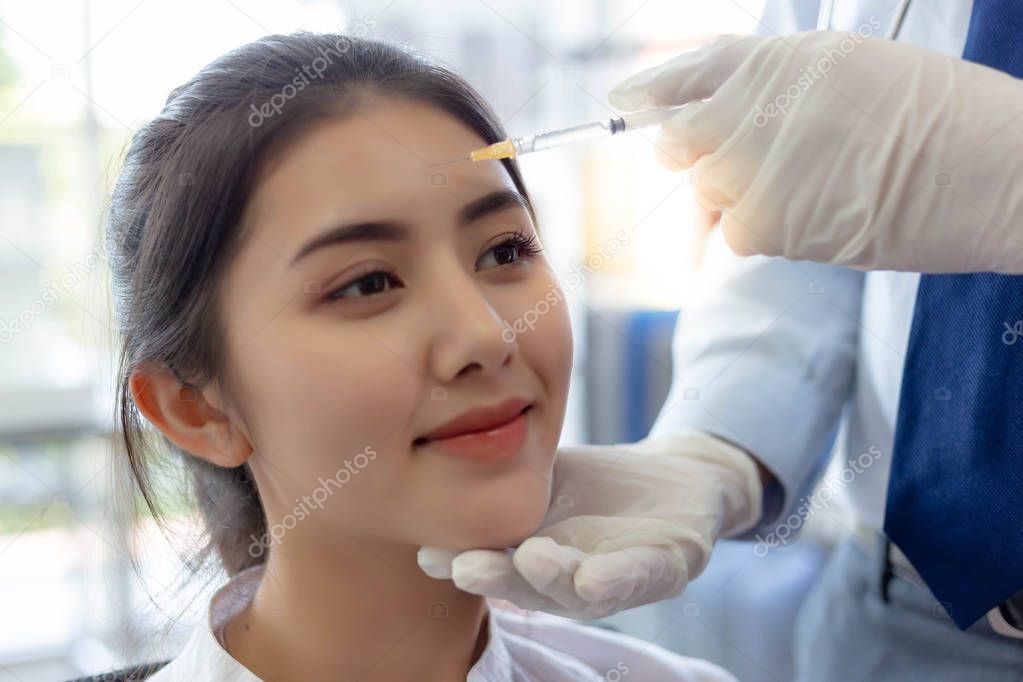 Charming beautiful woman or customer girl get satisfied and happy with quality of face lift at clinic of surgery when doctor inject Botulinum toxin A on forehead for reducing forehead line with smile