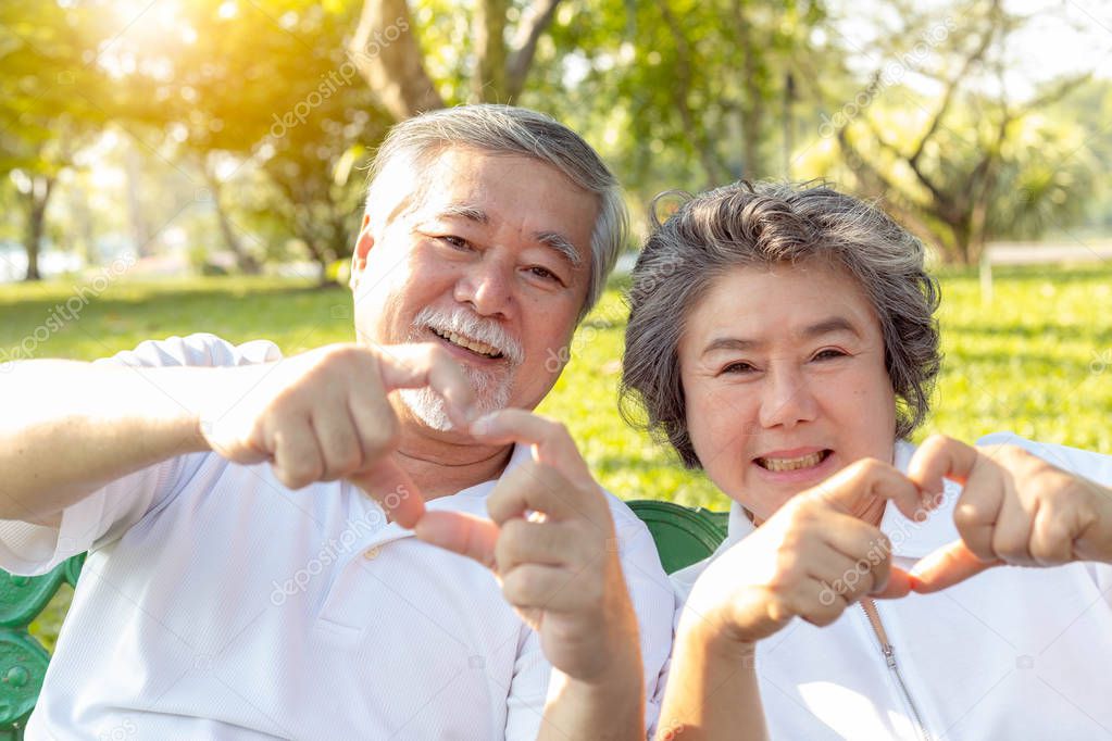 Grandma and grandpa or grandparents make symbol of love by using hands and fingers for making hearts. Lovely older couple or senior people love each other for long time. They give love to their family