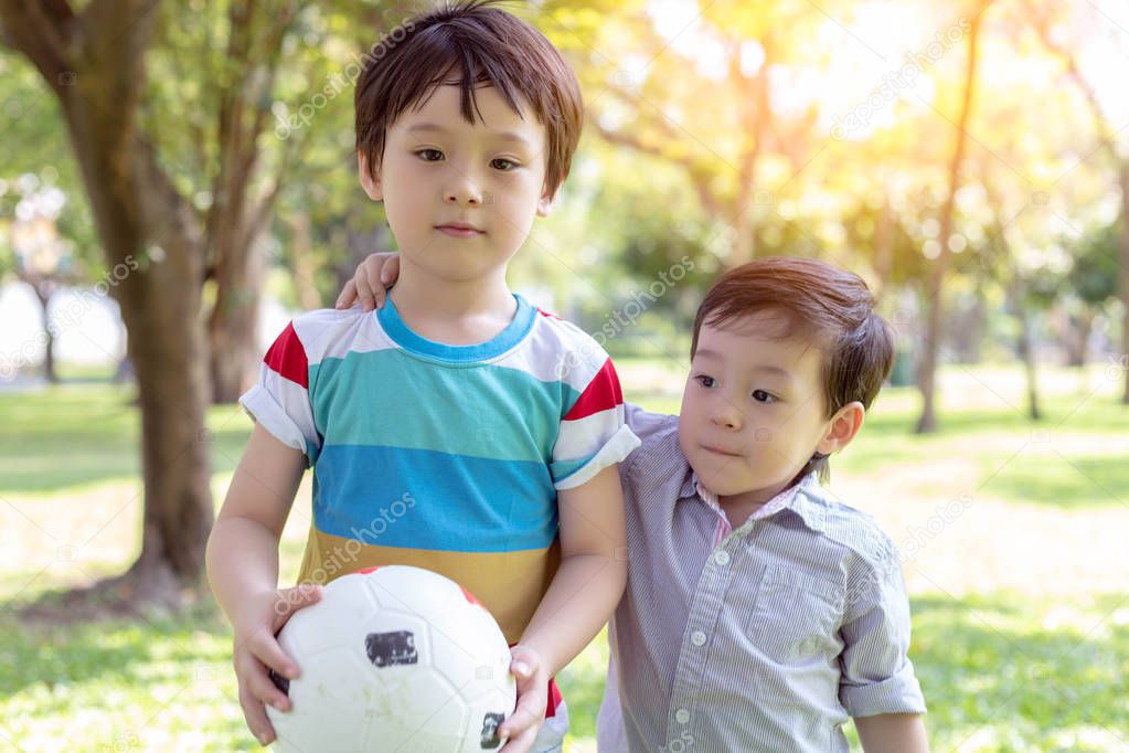 Handsome older brother holding ball and ready for playing in the park with younger brother. Little boy is always accompanied with his big brother and they always playing together. They love each other