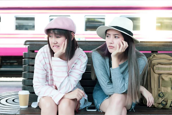 Beautiful asian traveler women waiting some taxi or bus to pick their up at train or bus station. Its arrival late. They feel boring and unhappy because she and friend are waiting for long time.