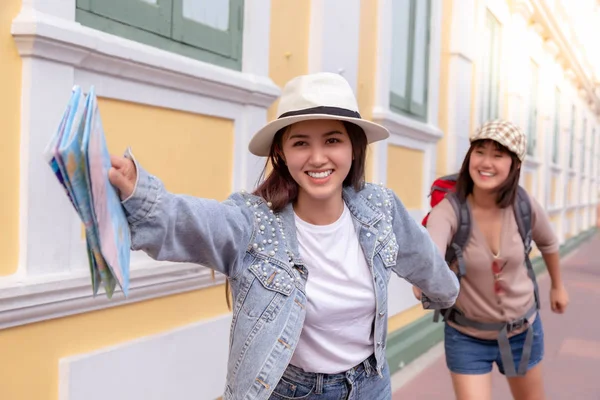 Charming beautiful traveler woman is holding hand friend and inviting friend to some touristic place. They look happiness and enjoy traveling in the beautiful city. Lovely women are running together