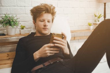 Yakışıklı genç işçi iş arama için yatağa akıllı telefon kullanarak. Cool adam olsun işsiz ve Web siteleri üzerinde çalışmak için bazı iş bulma. Yatak yatak odası, oturma. Genç adam evde yalnız kalmak
