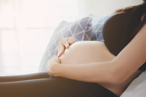 肖像画美しい妊婦。魅力的な美しいママは彼女の腹に触れ、彼女の胎児や赤ちゃんをチェックまたは検査するために医師を待っている間にベッドに座ります。妊娠中の女の子は来月出産します — ストック写真
