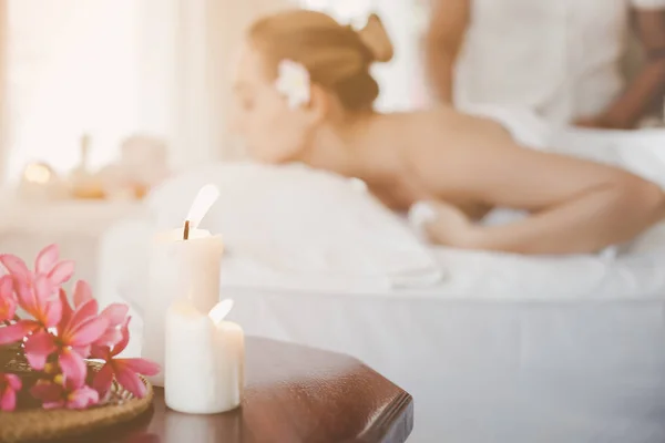 Belas velas na mesa na sala de spa com mulher bonita no salão de spa e fundo massagista ou massagista. Encantador bonito cliente mentira propenso a cama de spa para massagem em hotel de luxo — Fotografia de Stock