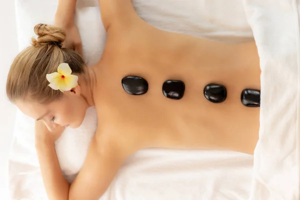 Mulher bonita fazendo terapia de pedra com pedras quentes no salão de spa e deitada na cama com os olhos fechados. Spa pedras pretas em suas belas costas. Mulher cliente lindo ficar tranquilo, relaxar e feliz — Fotografia de Stock