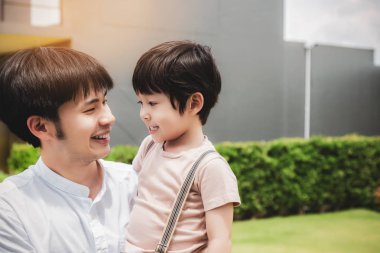 Mutlu aile konsepti. Baba ve oğul gülen yüzlerle birlikte bir yere gidiyor. Babam küçük sevimli çocuğu yanında taşır. Yakışıklı baba ve yakışıklı oğlu mutluluk düştü. Her zaman birlikte giderler.