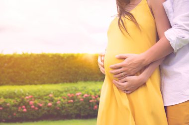 Koca kucaklayan veya kucaklayan karısı karın veya sevgi ile hamile kadın. Karısının karnında çocuk ya da fetüs var, romantik bir çift. Çift bir bebeğin sağlığının iyi olmasını bekler. güneş ışığı arka plan, kopyalama alanı