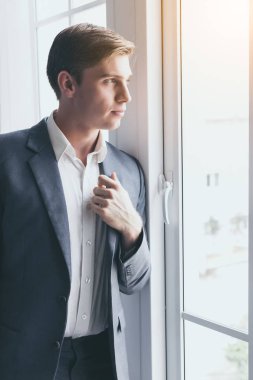 Yakışıklı genç iş adamı portresi. Çekici yakışıklı genç adam pencereden bakar ve ofiste birini bekler. Havalı adam güzel takım elbise, gömlek giyiyor. Zeki ve yakışıklı görünüyor.