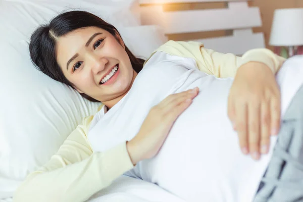快乐怀孕的年轻亚洲女人摸着肚子躺在床上 脸上挂着快乐的微笑 年轻的亚洲单身母亲非常爱她的孩子 妈妈等着要孩子 她的身体很健康 — 图库照片