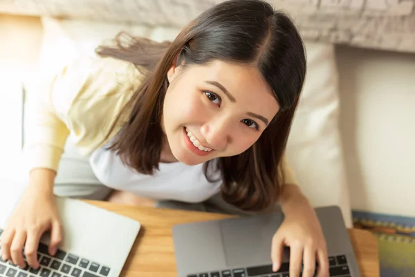 Asian Girl get new normal life, social distancing. Young businesswoman work at home by using laptop computer, video call, video conference with happiness and smiley face Pretty girl get relax top view