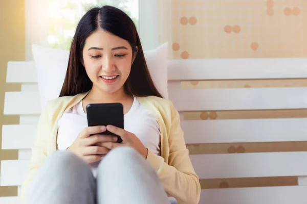 快乐的年轻亚洲女人在网上购物 网上银行 搜索信息 与朋友聊天 在床上发短信时面带微笑 — 图库照片