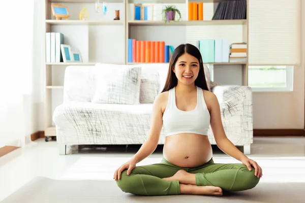 年轻的亚洲孕妇坐在客厅的瑜伽垫上 冥想瑜伽 怀孕的母亲在运动后会得到放松和快乐 这对母亲和婴儿以及产前护理都有好处 — 图库照片