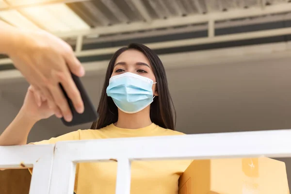 Woman signing on device to delivery parcel Asian woman receiving parcel box from delivery man in from of door at home. Beautiful girl wear face mask for protecting coronavirus. covid 19 concept