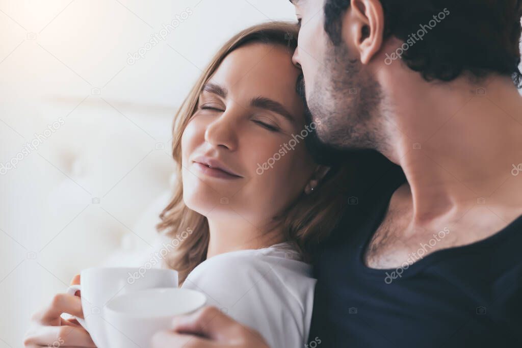 Beautiful woman lean on his body handsome man and couple spending time together on bed at home. Romantic couple get happiness with smile face. Husband kiss his wife romantic and in love couple concept