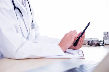 Tanımlanamayan doktor hastanedeki doktor ofisinde akıllı telefon kullanıyor, hastaya mesaj yazıyor, tedavi öneriyor. Online danışmanlık için doktor kullanımı ve hasta muayene sonuçları
