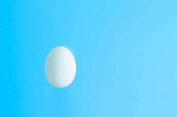 Single white egg isolated against light blue backdrop