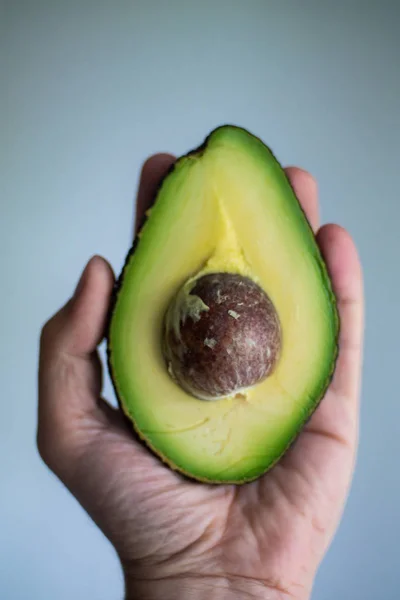 Half of freshly cut avocado with seed in male palm close up isol — Stock Photo, Image