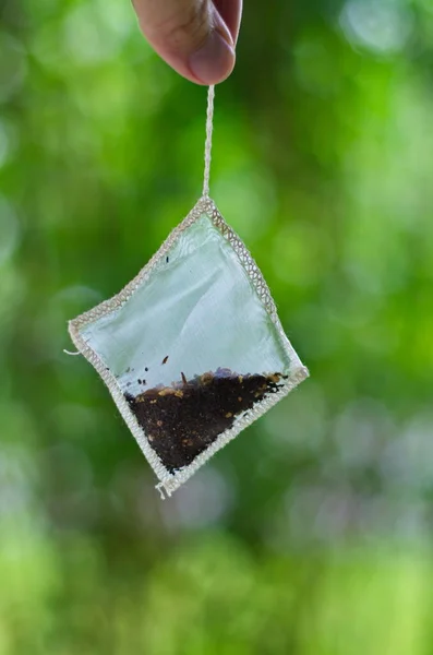 Dried leaf tea bag package hanging by a string held by Caucasian male hand isolated against green blurred background 2020