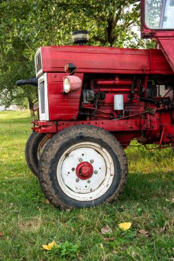 Yazın gün batımından önce çimlere park etmiş küçük kırmızı tarım traktörü. Üç çeyrek manzara..