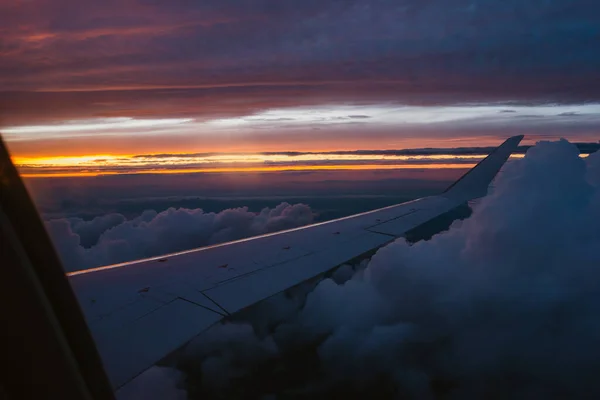 Airplane window view of dramatic cloudy colorful sunset.