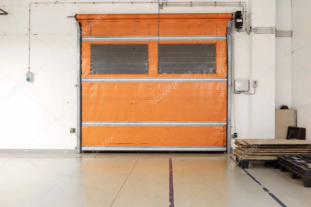 Orange warehouse shutter door close next to loading pallets interior point of view.
