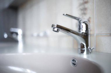 Daire banyosunun içinde parlak, krom su musluğu. Yakın çekim, sığ alan derinliği, insan yok.