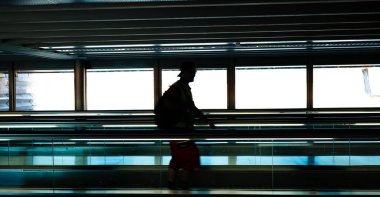 Havaalanı terminalinde yürüyen bir yolda ya da yürüyen merdivende tanımlanamayan bir adam silueti. Geniş açı görünümü, arka ışıklandırma, karamsar ışık
