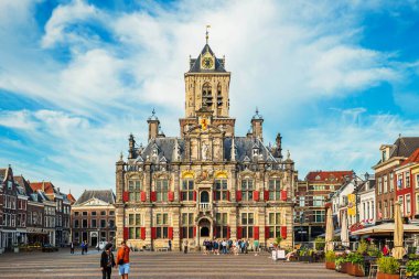 Delft, Hollanda, 26 Ağustos 2025. Kasaba meydanındaki turistler ve yerliler güzel eski belediye binasına bakıyor. Bulutlu güneşli yaz günü, geniş açı manzaralı.