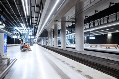 Delft, Hollanda, 26 Ağustos 2025. Yeraltı ana istasyon peronunda banklar ve trende bekleyen insanlar var. Geniş açı görünümü, yapay tavan aydınlatması