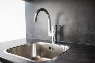 Closed, new, stainless water tap faucet and sink in apartment kitchen. Bright, natural window light, selective focus, no people