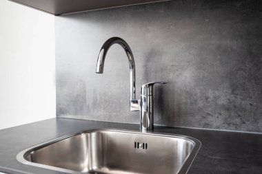 Closed, new, stainless water tap faucet and sink in apartment kitchen. Bright, natural window light, selective focus, no people