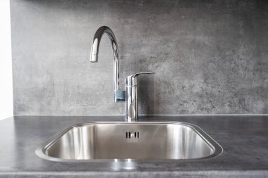 Closed, new, stainless water tap faucet and sink in apartment kitchen. Bright, natural window light, selective focus, no people