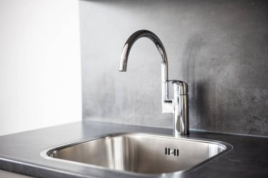 Closed, new, stainless water tap faucet and sink in apartment kitchen. Bright, natural window light, selective focus, no people