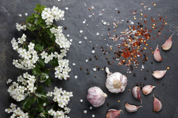 Early summer white  flower blossoms with pink garlic and Himalayan rock salt with pepper and chilli on slate